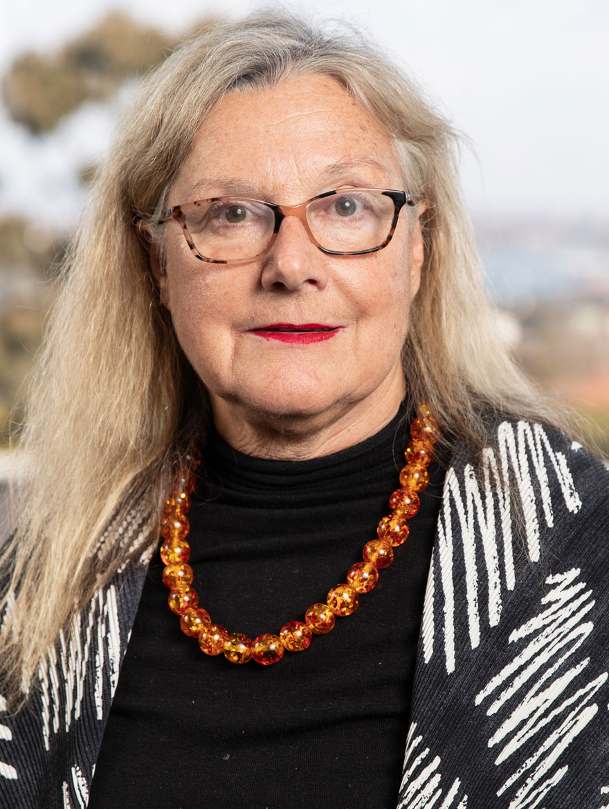 An older woman with long blonde hair wearing an orange bead necklace.